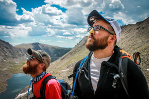 Two bearded male hikers looking up to the sky. Both men have their noses covered in Nöz reef safe sunscreen. 